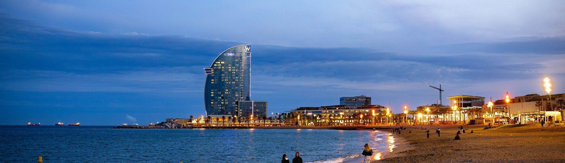 Barceloneta beach at dusk, with the W Hotel and the seafront lights coming on