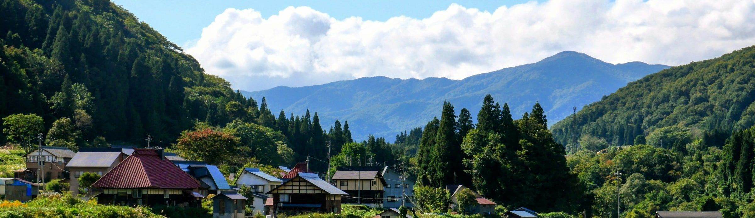 A rural Japanese village in a lush green mountain valley under blue sky