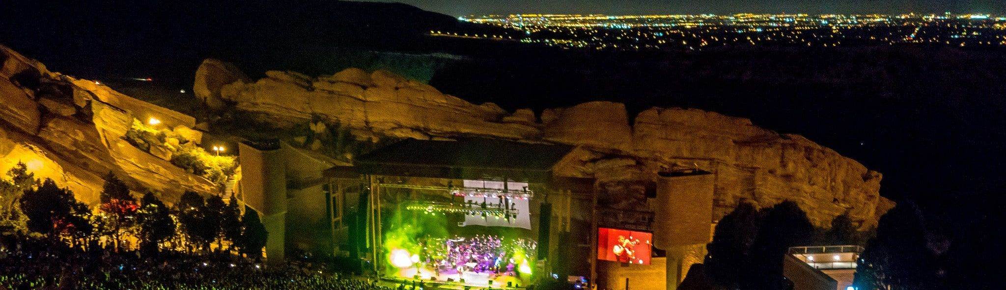 A night concert at Red Rocks Amphitheatre, the stage lit up between the sandstone rocks, with city lights beyond